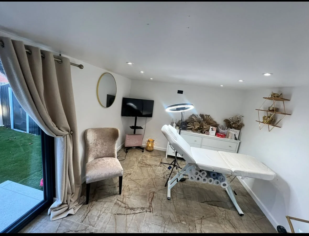 Beauty and treatment room with a treatment bed, seating, fitted flooring and wide glazed doors