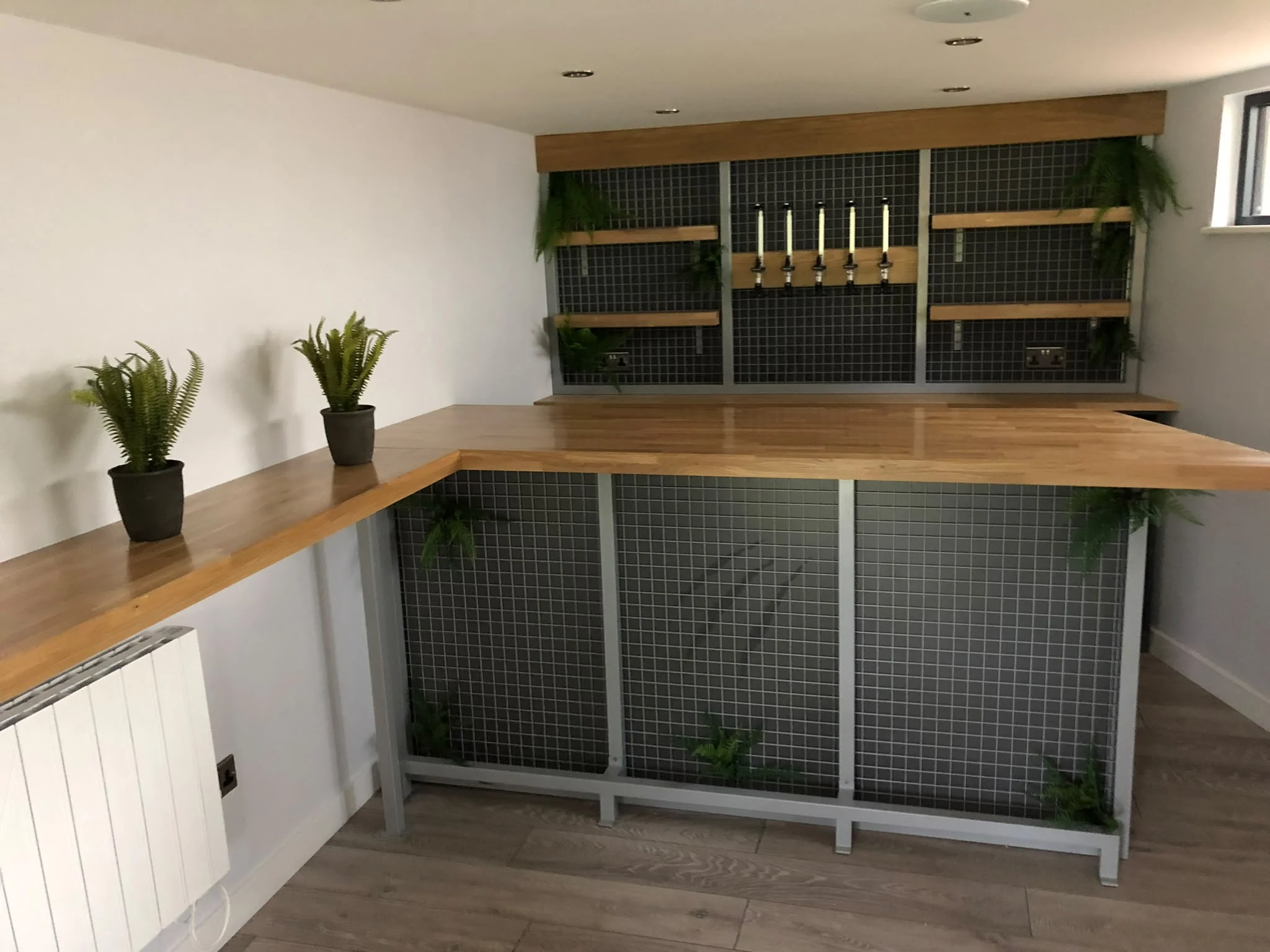 Bespoke garden bar with timber worktops, dark mesh panels and fitted shelving