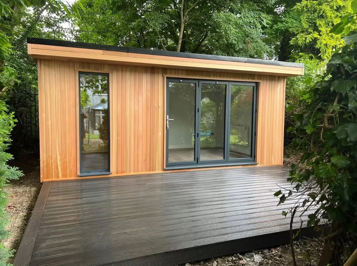 Timber garden room with dark-framed glazing and a generous deck surrounded by trees