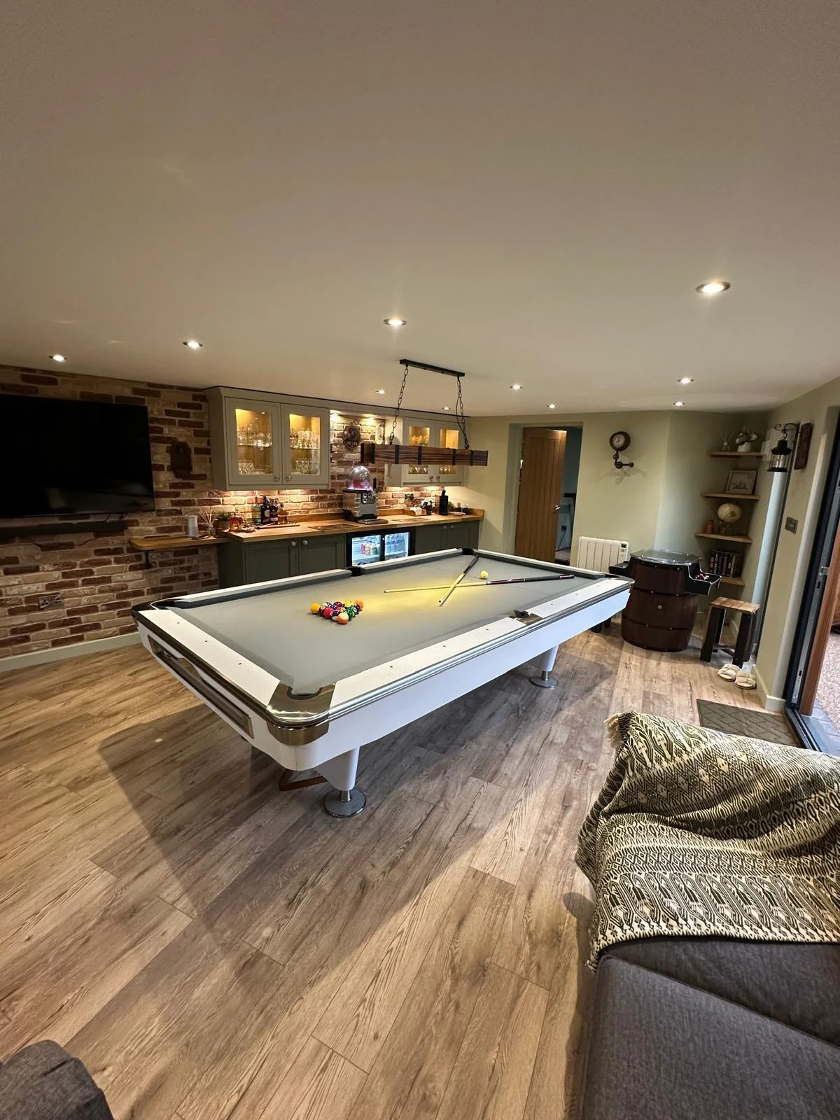 Finished garden games room with a pool table, fitted bar, timber-effect flooring and seating