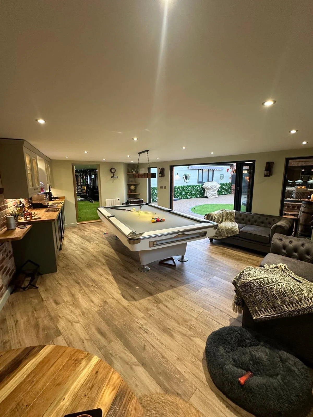 Finished garden room with a pool table, seating, timber-effect flooring and wide doors to the garden