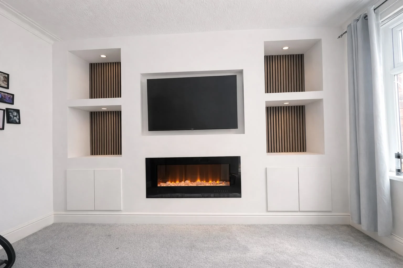 Completed white media wall with a television, recessed shelving, timber slat details and an inset fireplace